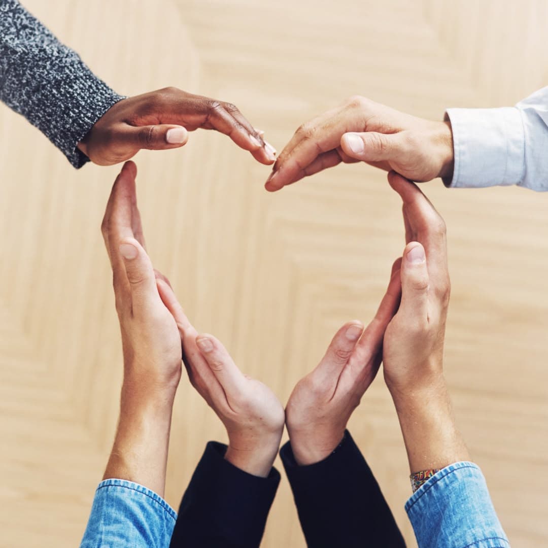 Six hands from different people meeting to form the outline of a heart.