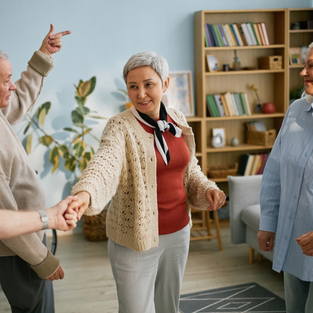 Older adults dancing together in a bright communal living room.