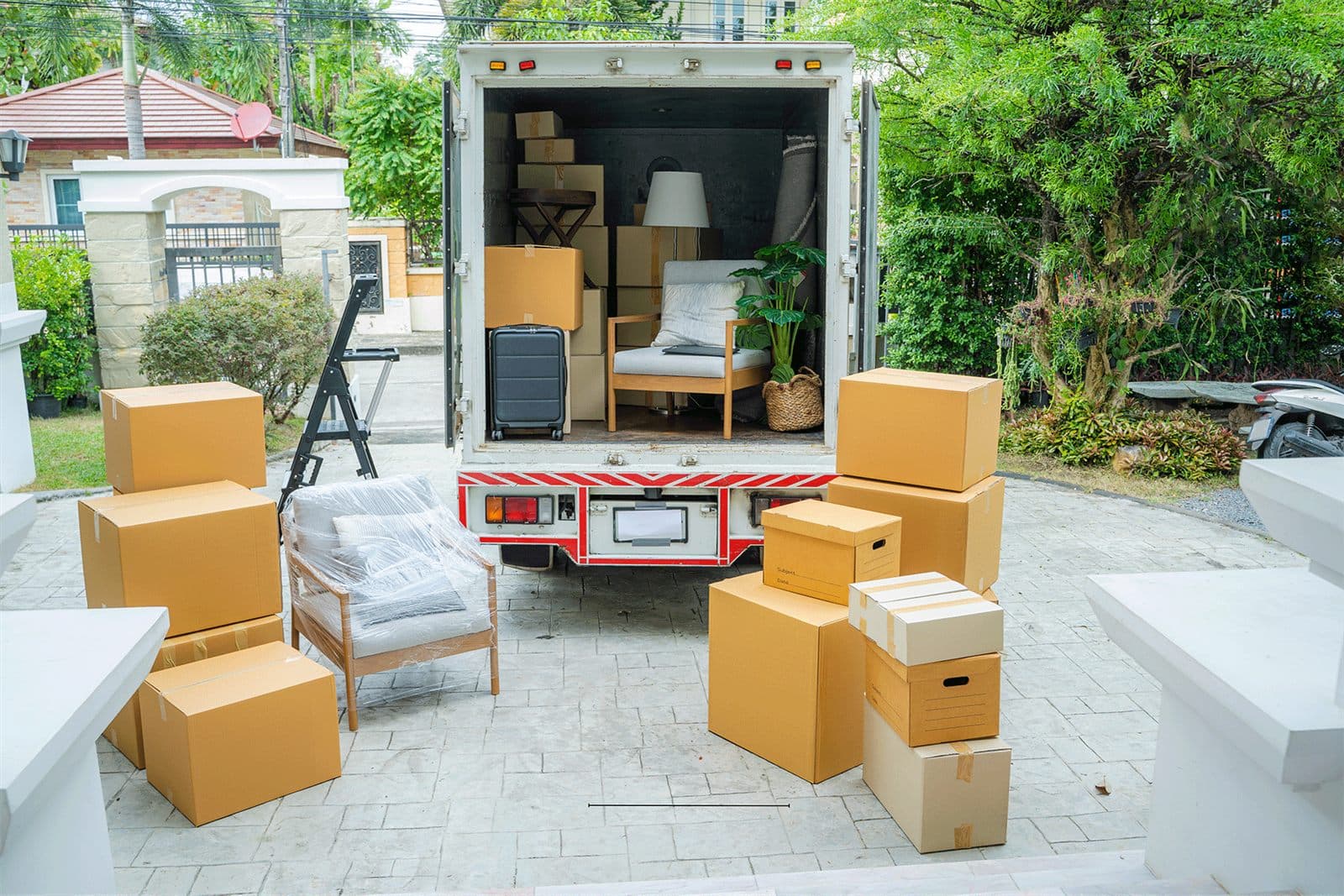 Cardboard boxes and furniture stacked on a driveway beside an open moving truck.