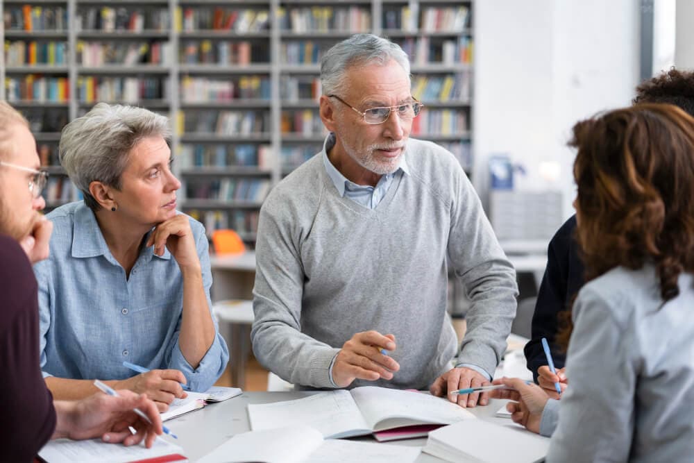 Several older adults seated around a table with notebooks, talking things through with an adviser.