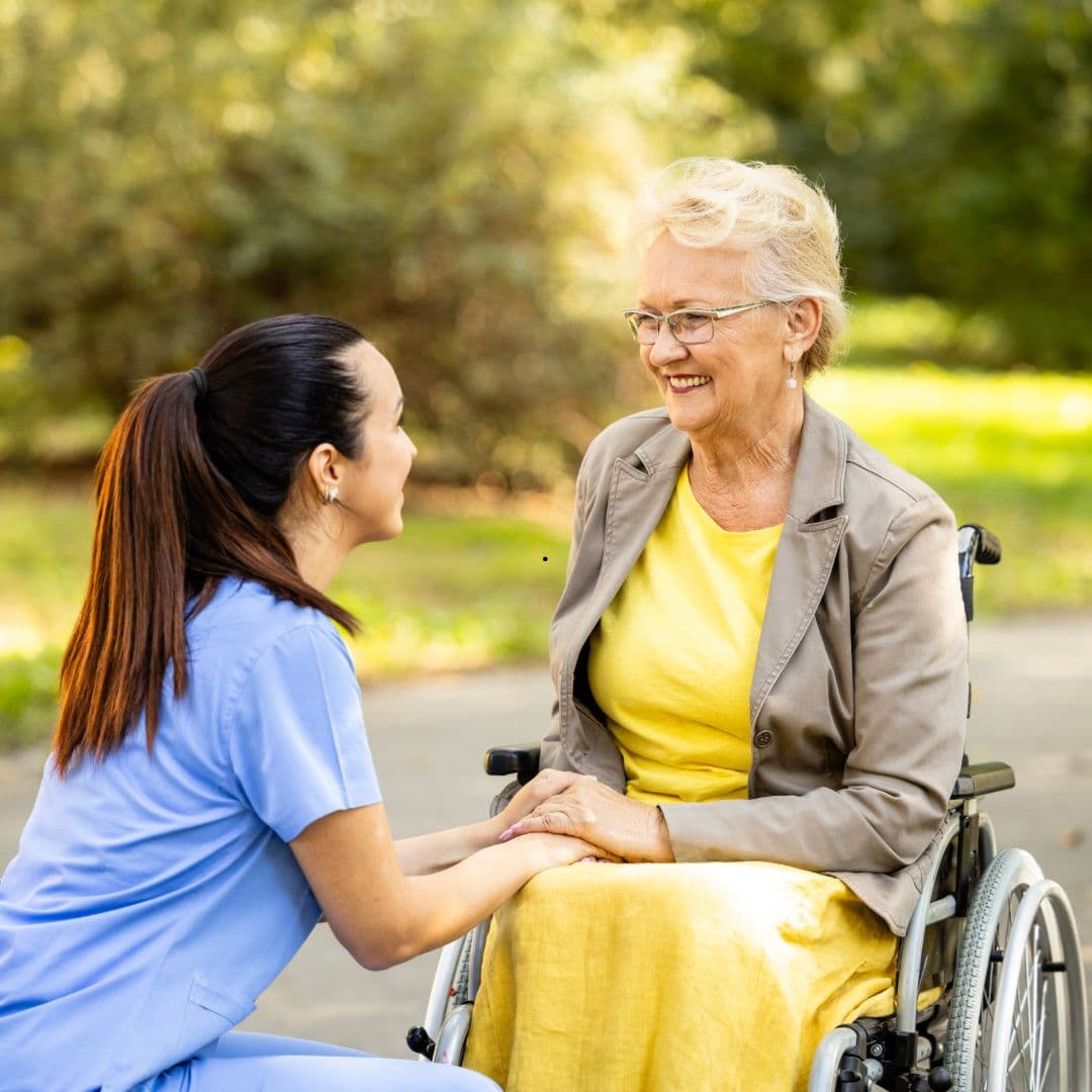 A care worker walking outdoors beside an older man, talking with him.